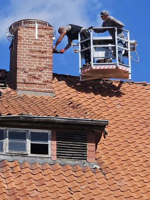 Montage eines Storchenhorstes in Dörmte Zwei Männer stehen auf einer Hebebühne und befestigen ein künstliches Storchennest auf dem Schornstein eines Ziegeldachs